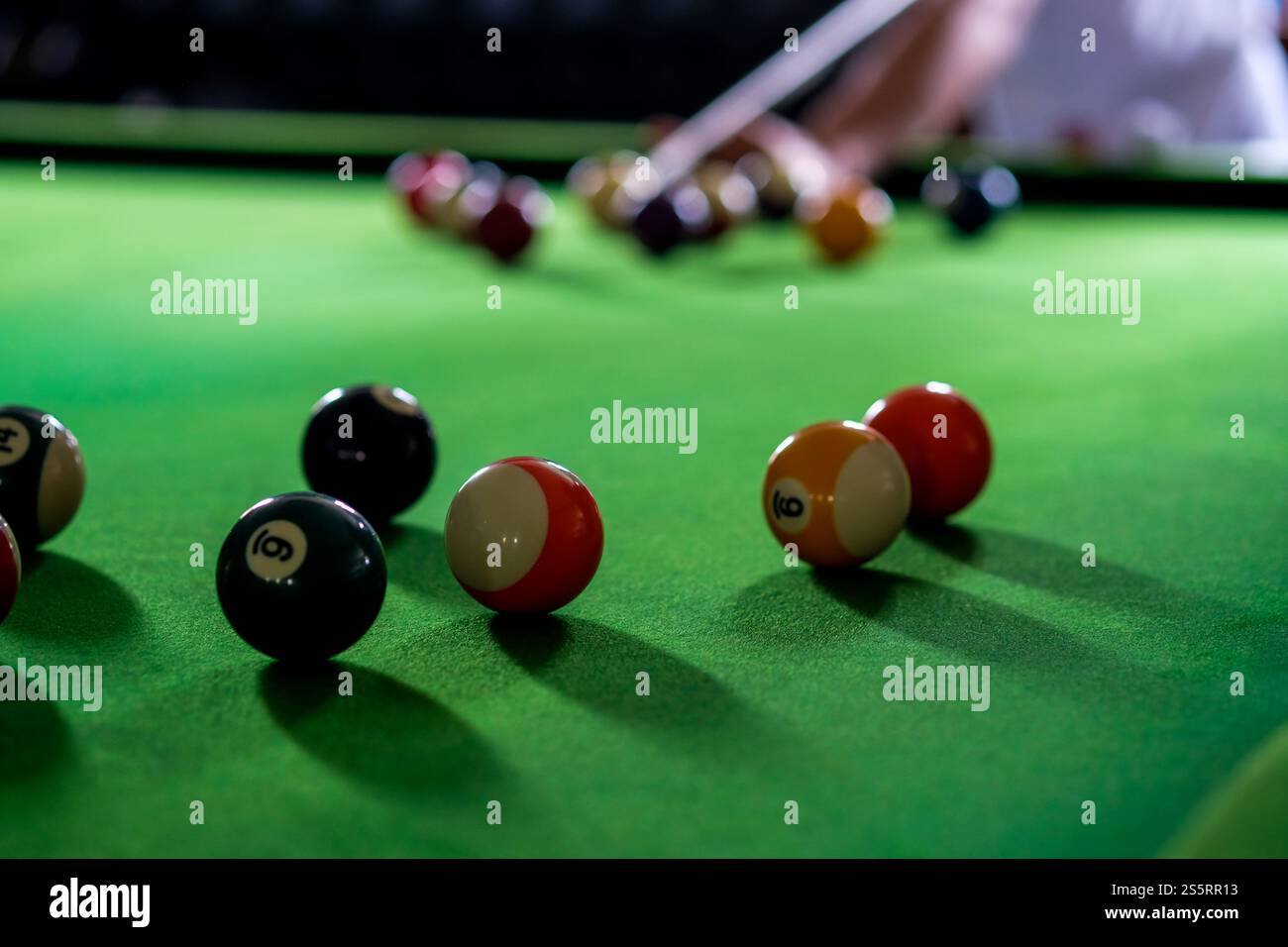 Mans mano e braccio cue giocano a biliardo o si preparano a sparare palle da biliardo su un tavolo da biliardo verde. Palline da biliardo colorate sul fregio verde Foto Stock