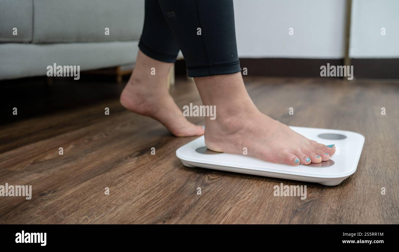 piedi in piedi su bilance elettroniche per il controllo del peso. Strumento di misurazione in chilogrammi per il controllo della dieta. Foto Stock