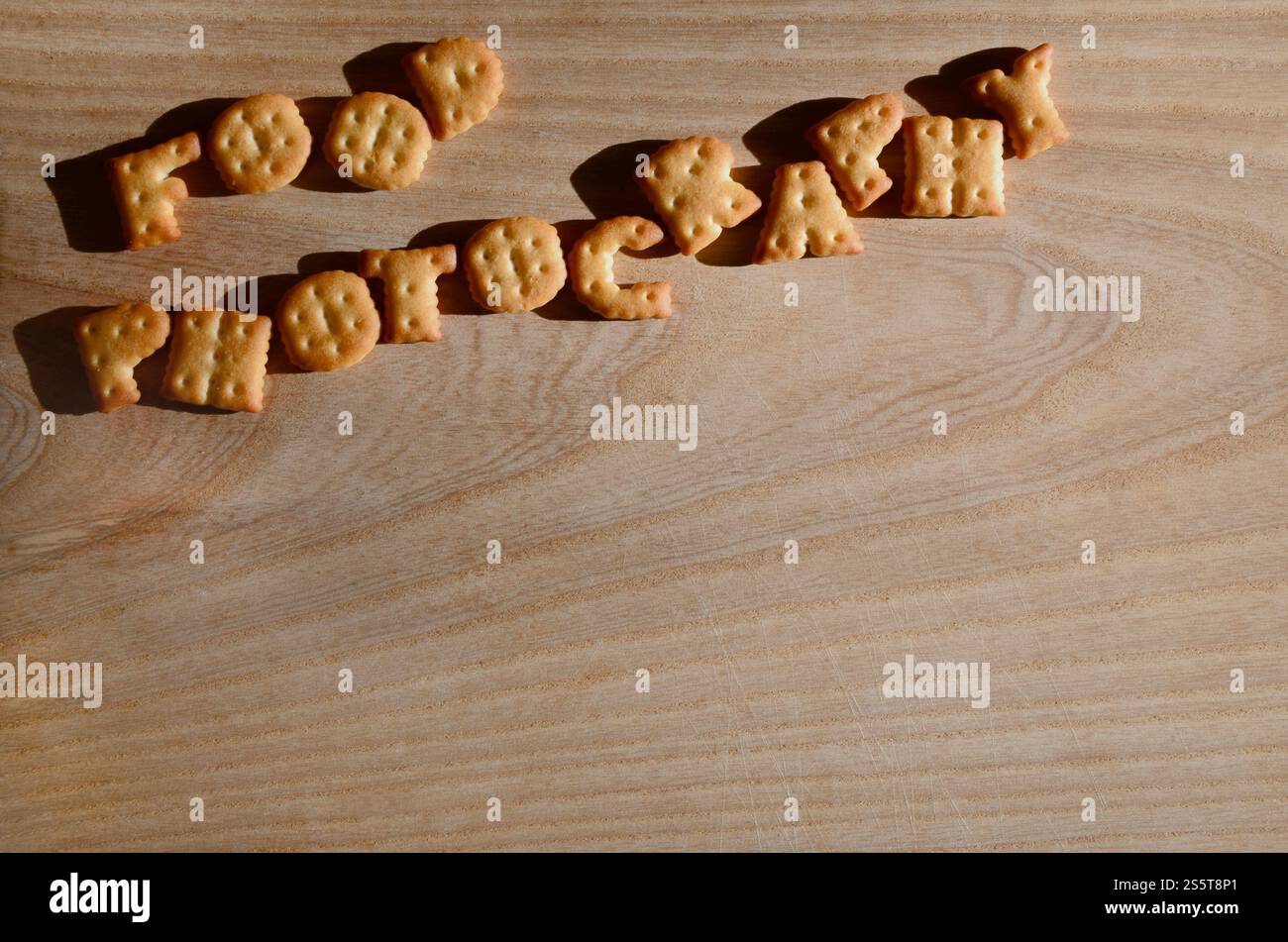 Fotografia gastronomica. Testo dai cracker salati come lettere inglesi stampate che giacciono su un tagliere di legno. Messaggio, fiancheggiato da lettere commestibili. Foto Stock