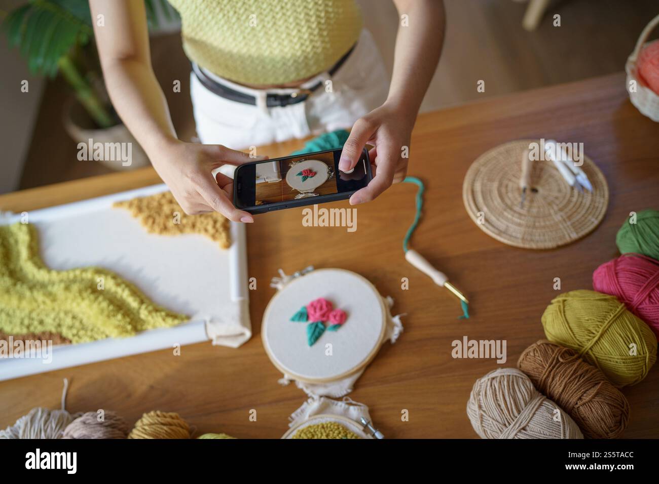 Donna asiatica che scatta foto smartphone Punch Needle. postazioni telefoniche sui social network in officina. Ambiente di lavoro di design progetto artigianale fai da te Foto Stock
