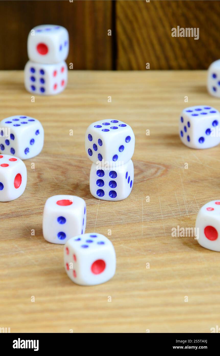Alcuni dadi giacciono sulla superficie di legno naturale. Elementi per generare numeri da uno a sei sotto forma di punti dipinti sul lato di Foto Stock