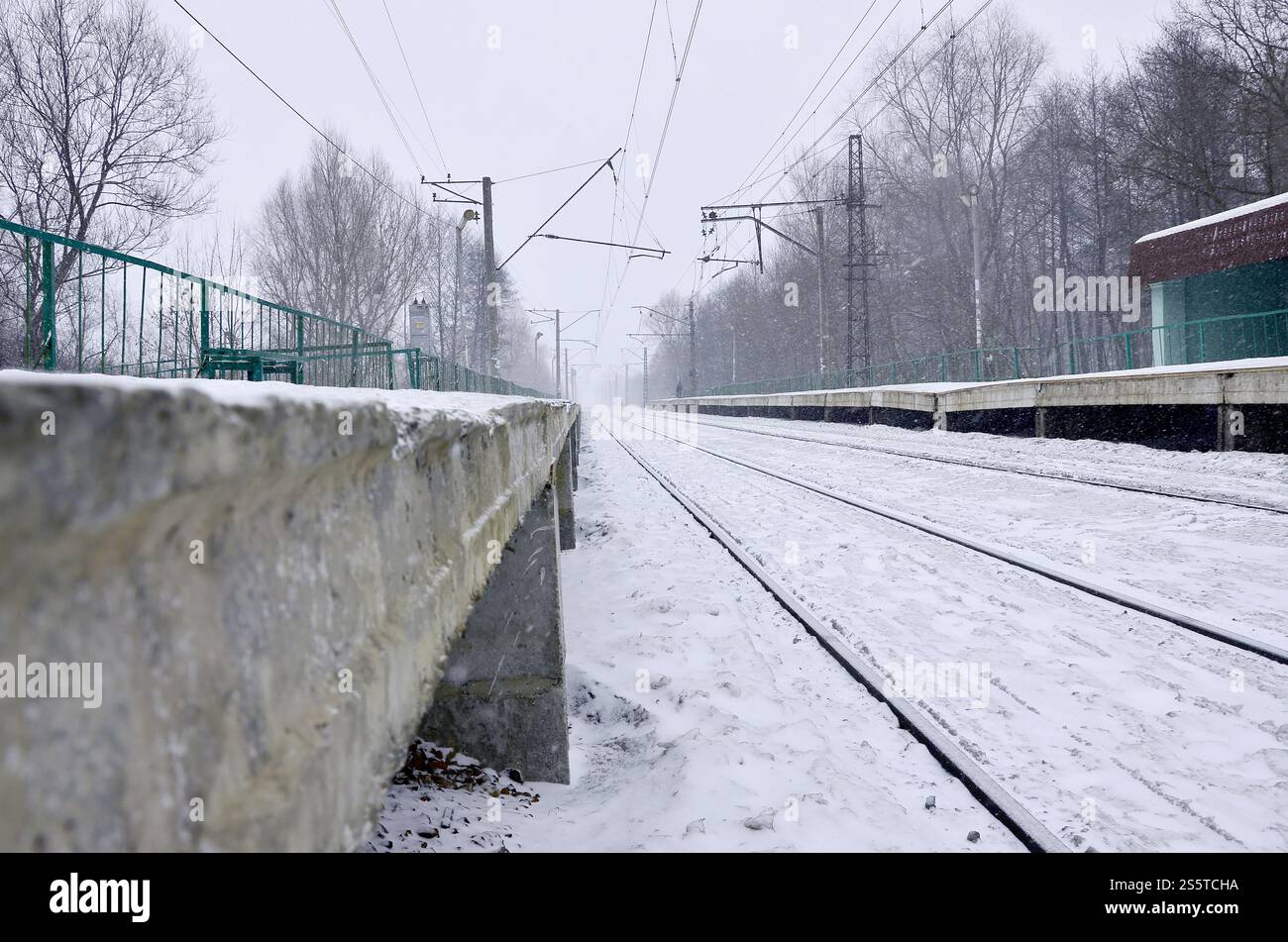 Stazione ferroviaria vuota in forte nevicata con fitta nebbia. Le rotaie si spengono in una nebbia bianca di neve. Il concetto di trasporto ferroviario in inverno. Foto Stock