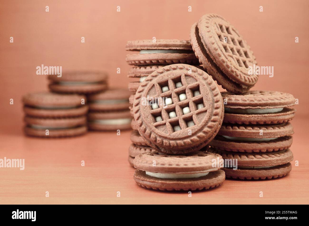 Un mucchio di biscotti con scaglie di cioccolato ripieni di crema bianca alla vaniglia giace su una superficie marrone di legno. Panini dolci e gustosi con biscotti rotondi. Cibo dettagliato Foto Stock