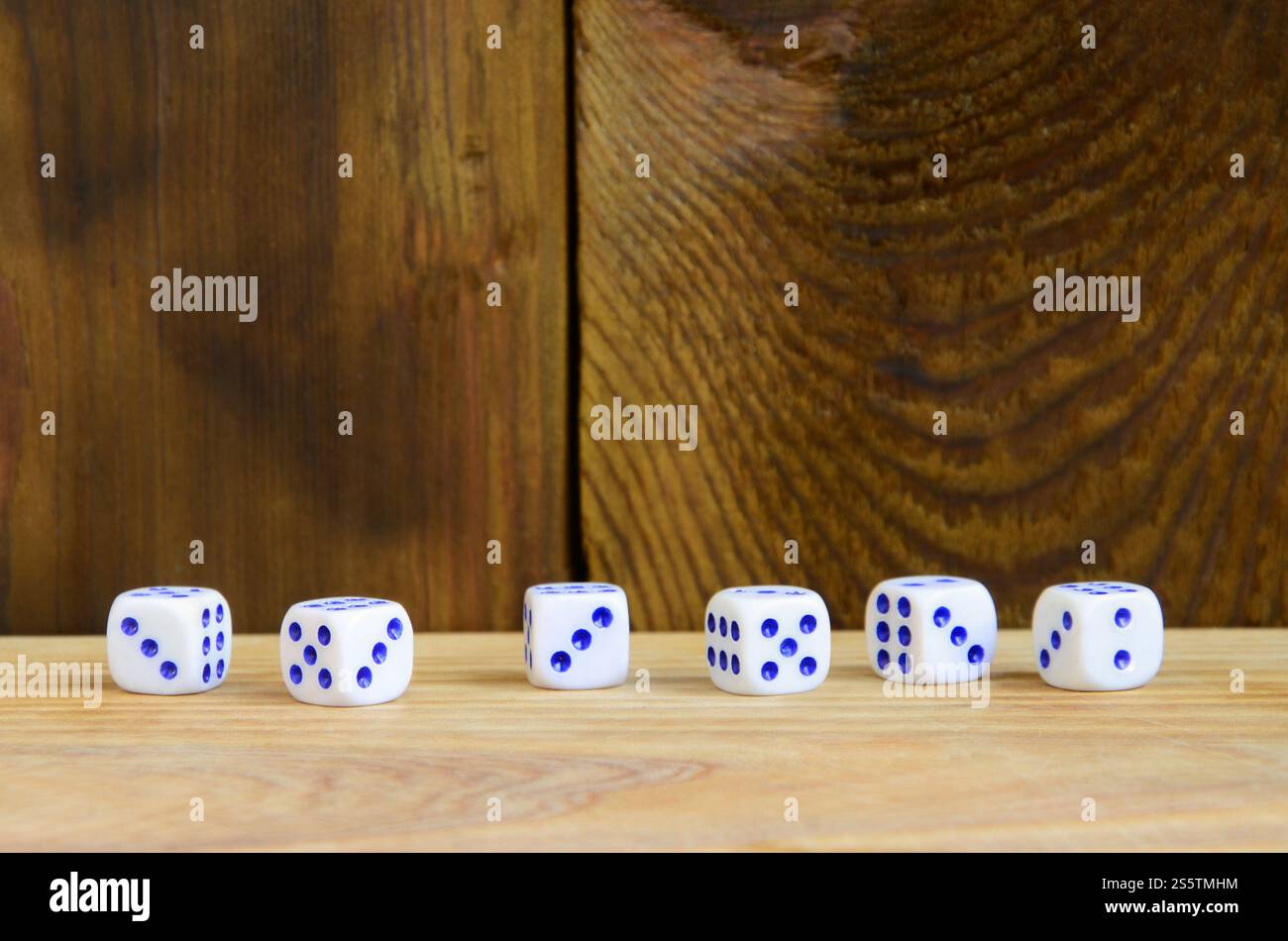 Alcuni dadi giacciono sulla superficie di legno naturale. Elementi per generare numeri da uno a sei sotto forma di punti dipinti sul lato di Foto Stock