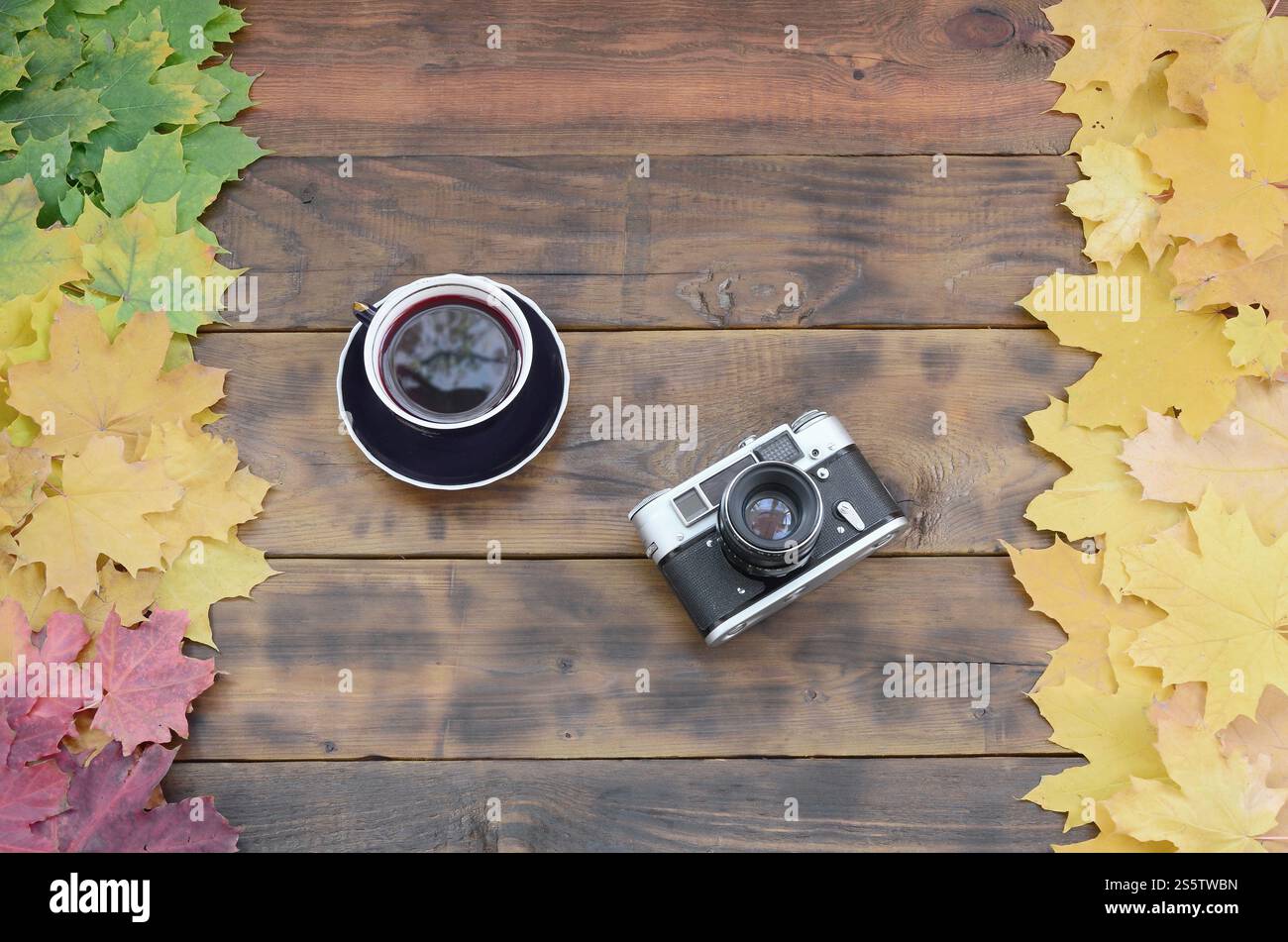Una tazza di tè e una vecchia macchina fotografica tra un insieme di fenomeni di ingiallimento caduto foglie di autunno su una superficie di sfondo di naturale di tavole di legno di colore marrone scuro Foto Stock