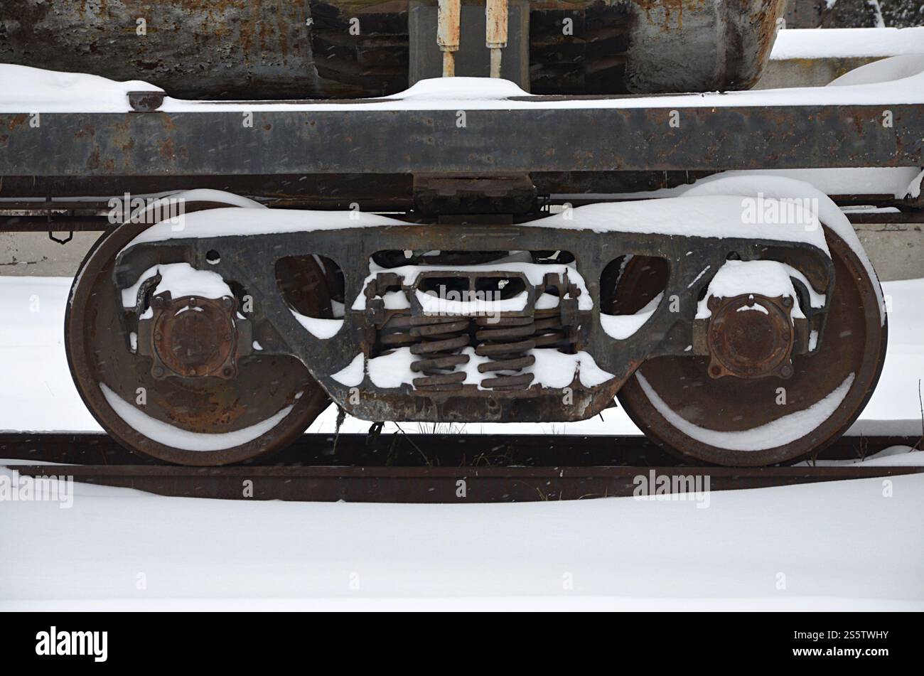 Foto dettagliata di un vagone ferroviario ghiacciato innevato. Un frammento dei componenti della vettura merci sulla ferrovia nelle nevose serali invernali. Foto Stock