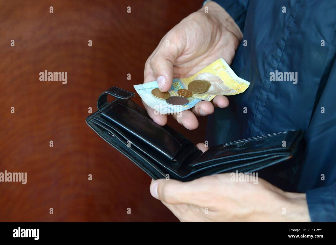 Una mano maschile con monete con piccole banconote ucraine e una vecchia borsa nera. Concetto di un piccolo budget e povera vita ucraina. Crisi economica. Un maschio Foto Stock