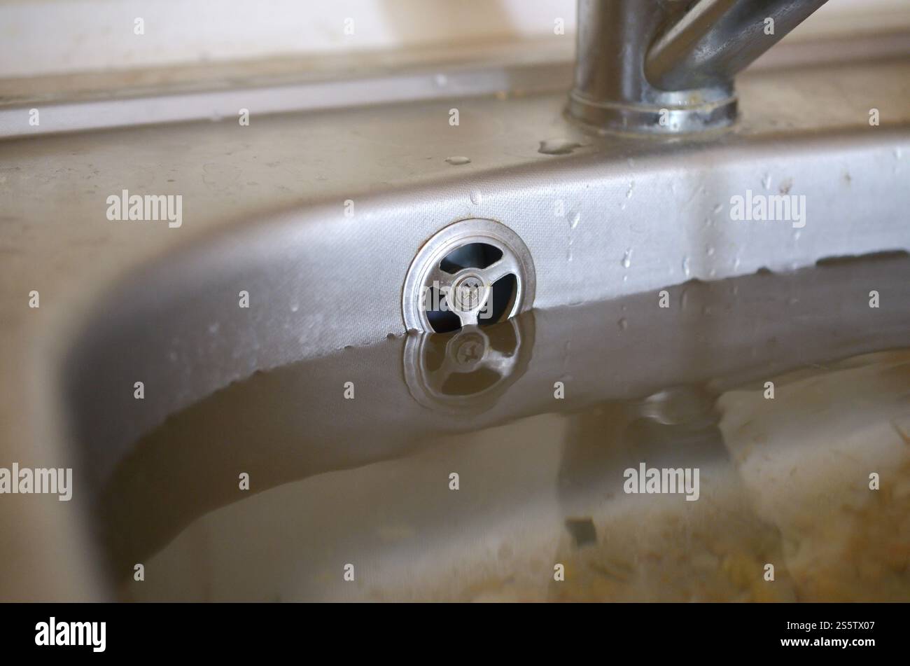 Il foro del tappo del lavandino in acciaio inox si chiude pieno di acqua e particelle di cibo. Lavandino da cucina traboccante, scarico intasato. Problemi con l'approvvigionamento idrico. Foto Stock