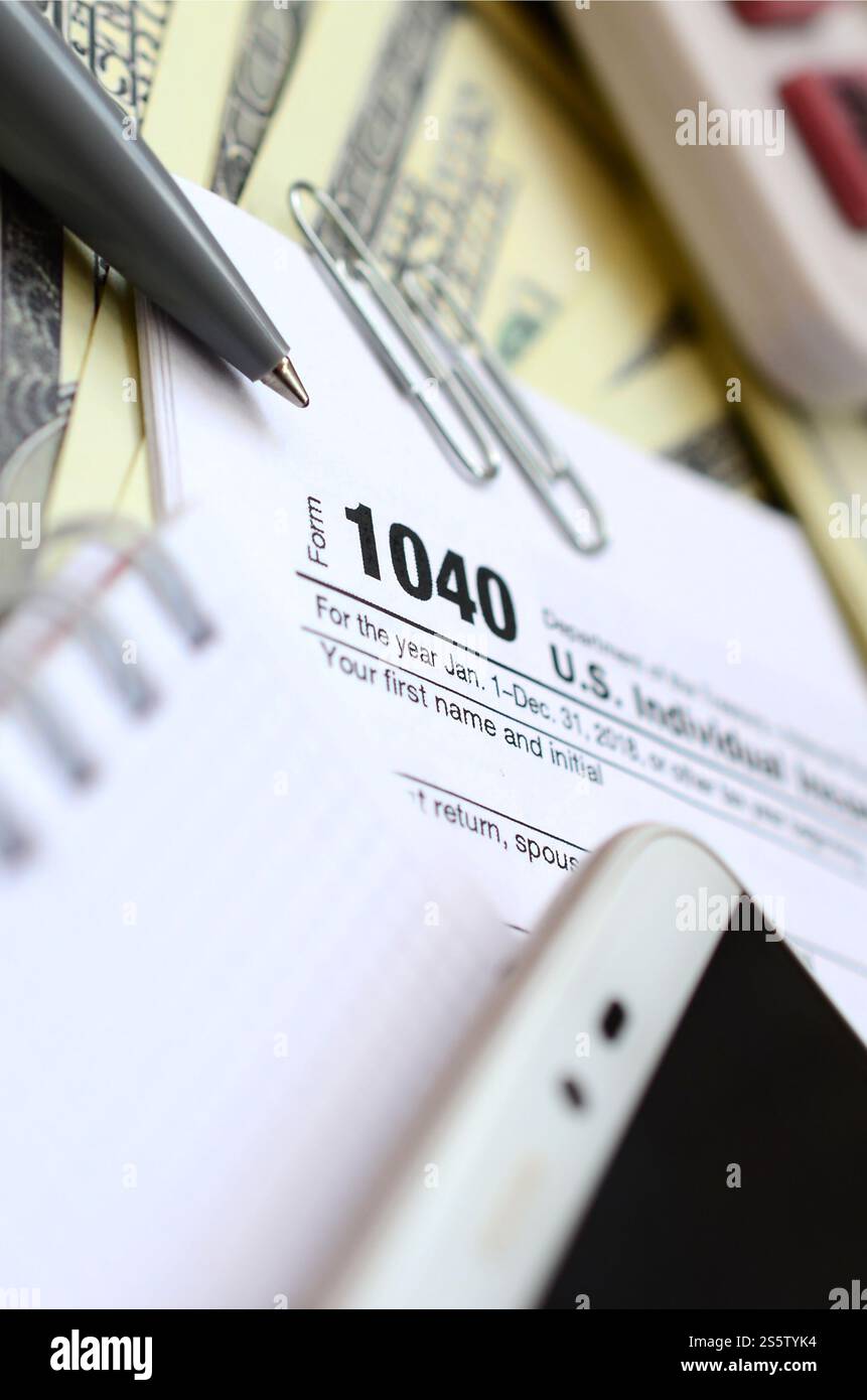 La penna, il notebook, la calcolatrice, lo smartphone e le fatture del dollaro si trova sul modulo di imposta 1040 US Reddito Individuale ritorno di imposta. Il tempo di pagare le tasse Foto Stock