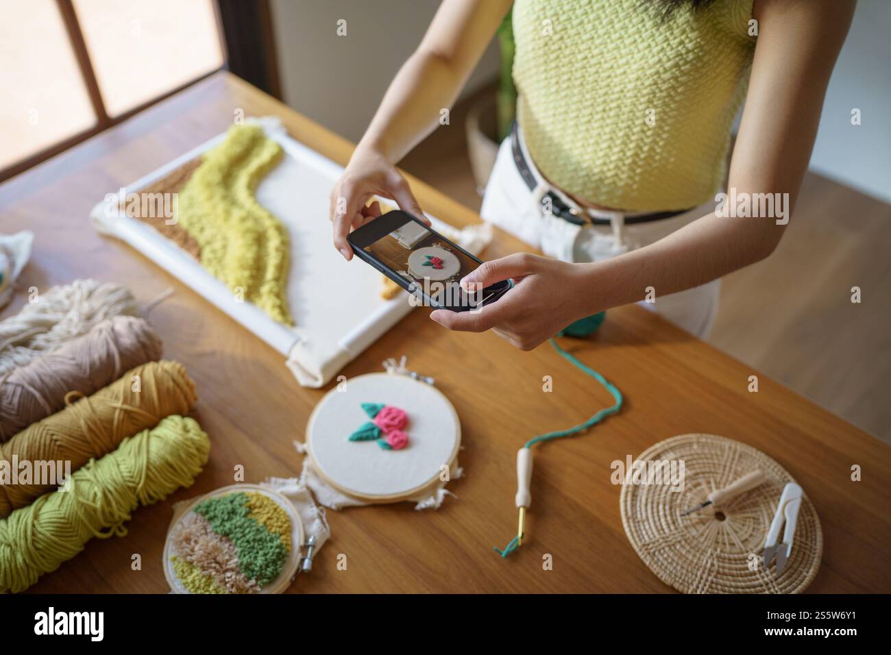 Donna asiatica che scatta foto smartphone Punch Needle. postazioni telefoniche sui social network in officina. Ambiente di lavoro di design progetto artigianale fai da te Foto Stock