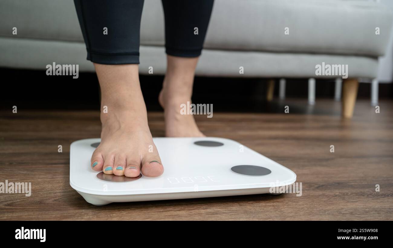 piedi in piedi su bilance elettroniche per il controllo del peso. Strumento di misurazione in chilogrammi per il controllo della dieta. Foto Stock