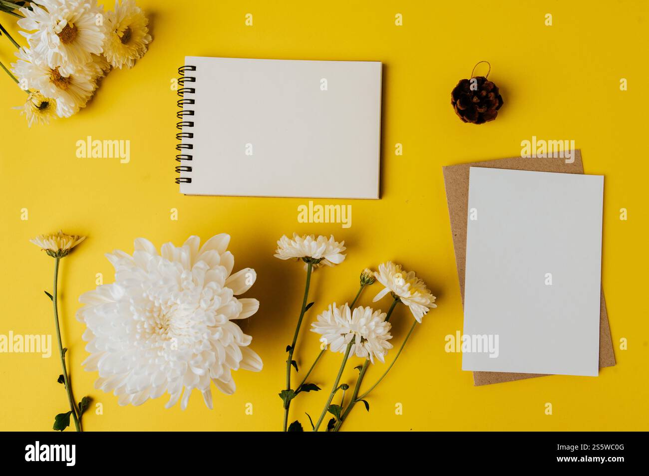 il quaderno e il cartoncino bianco con fiori sono posizionati su sfondo giallo Foto Stock