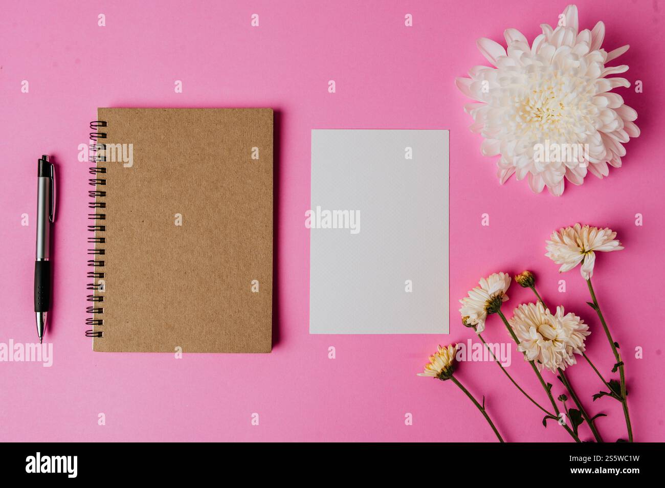 blocco appunti, penna, scheda vuota e fiore su sfondo rosa Foto Stock