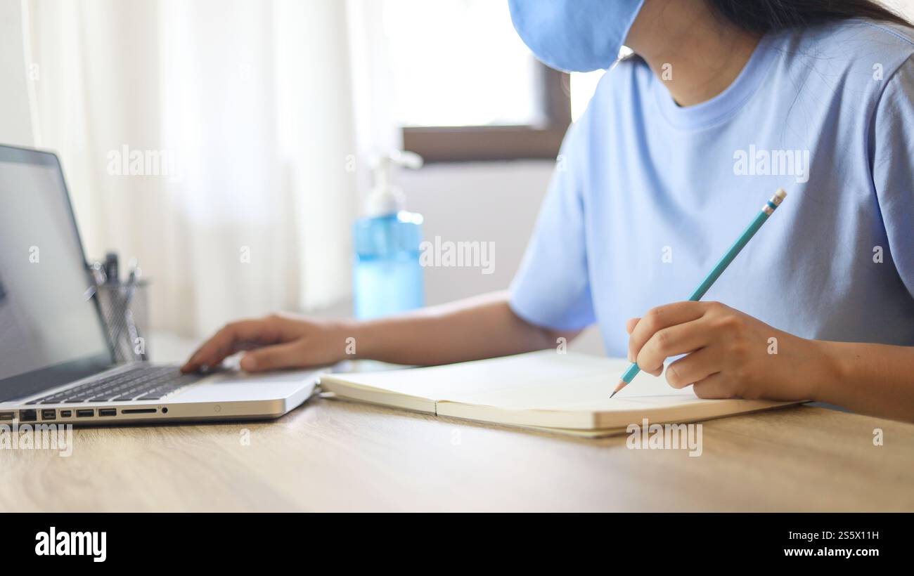 Giovane donna asiatica che indossa maschera facciale medica fatta a mano che lavora da sola distanziando politica con. Gel igienizzante per le mani durante il coronavirus o il virus covid-19 Foto Stock