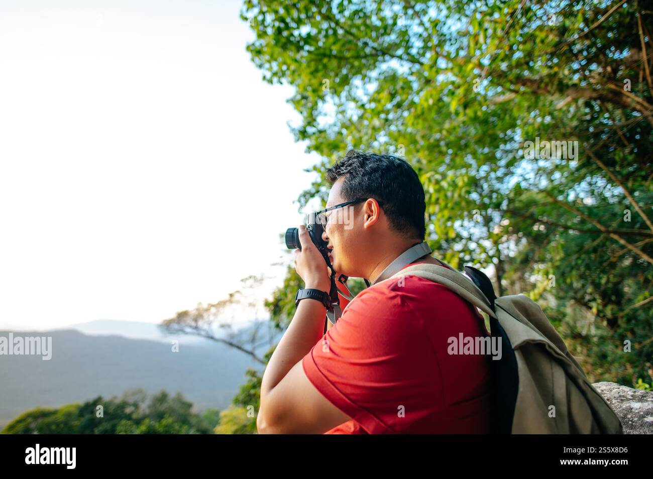 Vista laterale di Young trekking man con occhiali da vista in piedi e utilizzare la fotocamera per scattare foto splendida vista dal punto di vista, copia spazio Foto Stock