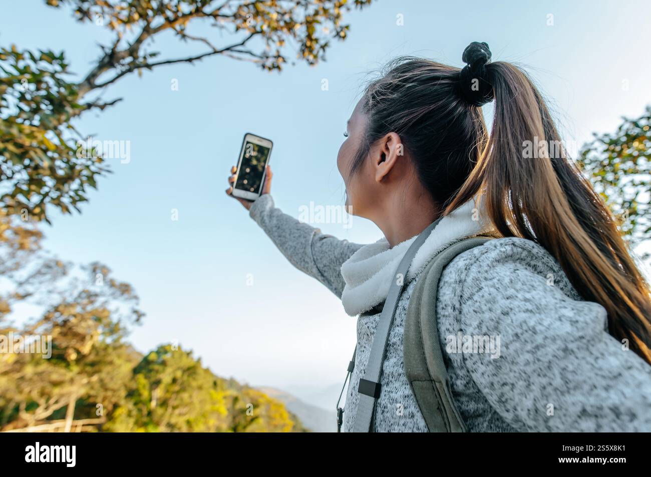 Vista laterale di Young trekking Woman con occhiali da vista in piedi e utilizza selfie su smartphone con una splendida vista dal punto di vista, copia spazio Foto Stock