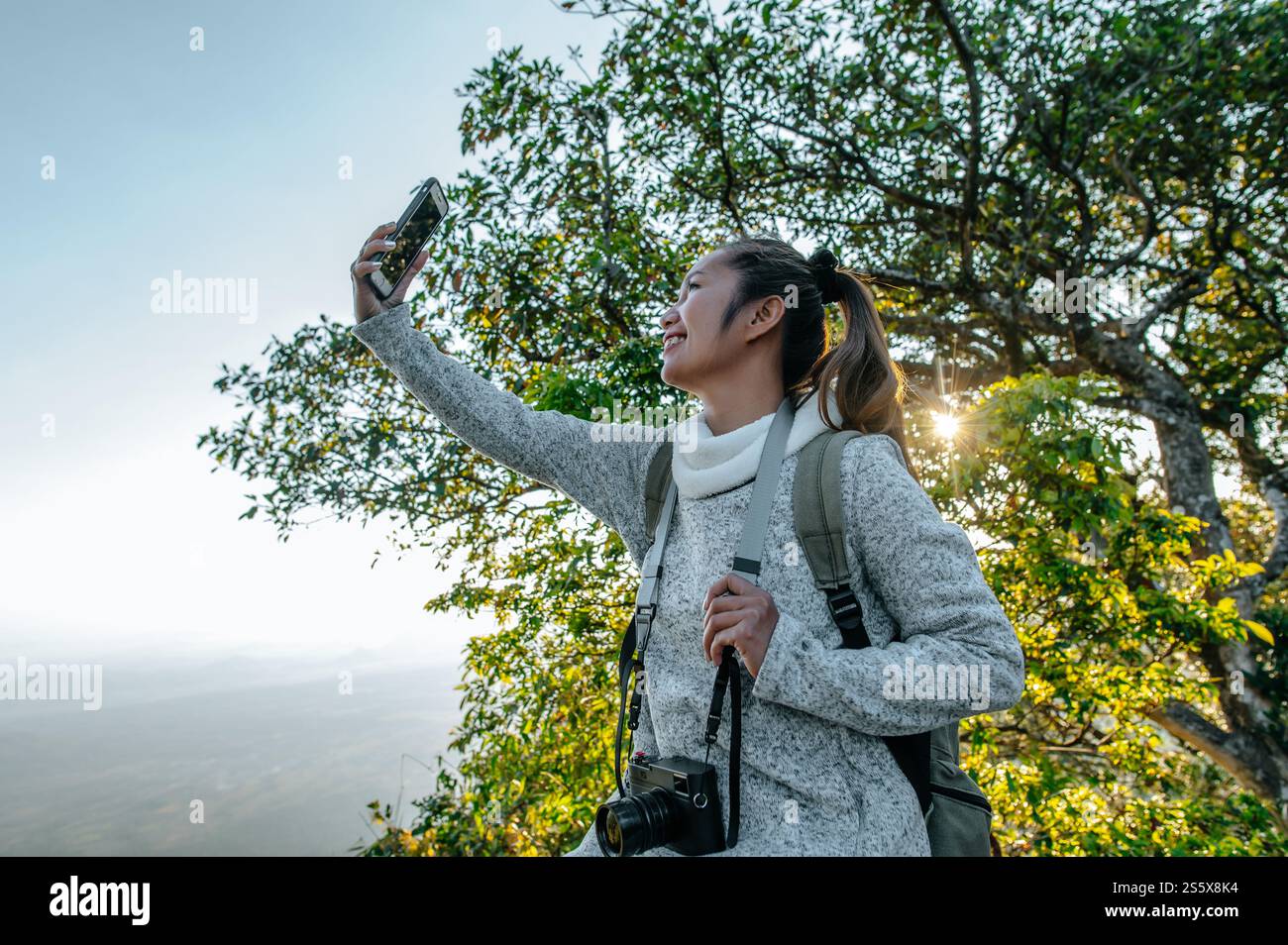 Vista laterale di Young trekking Woman con occhiali da vista in piedi e utilizza selfie su smartphone con una splendida vista dal punto di vista, copia spazio Foto Stock