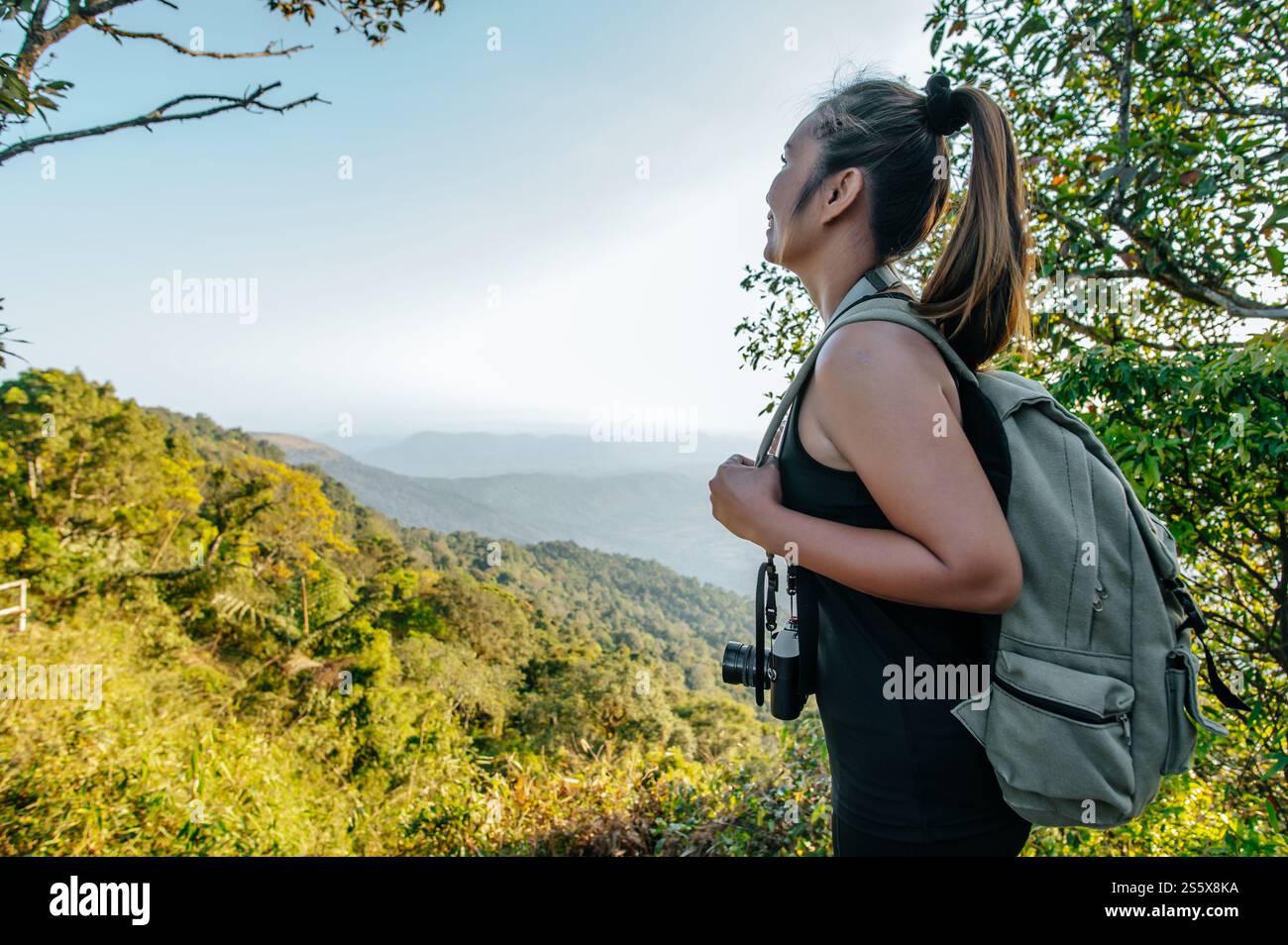 Vista laterale giovane donna asiatica che si trova in piedi al punto panoramico e che guarda una splendida vista con felice sulla montagna di picco e raggi del sole, copia spazio Foto Stock