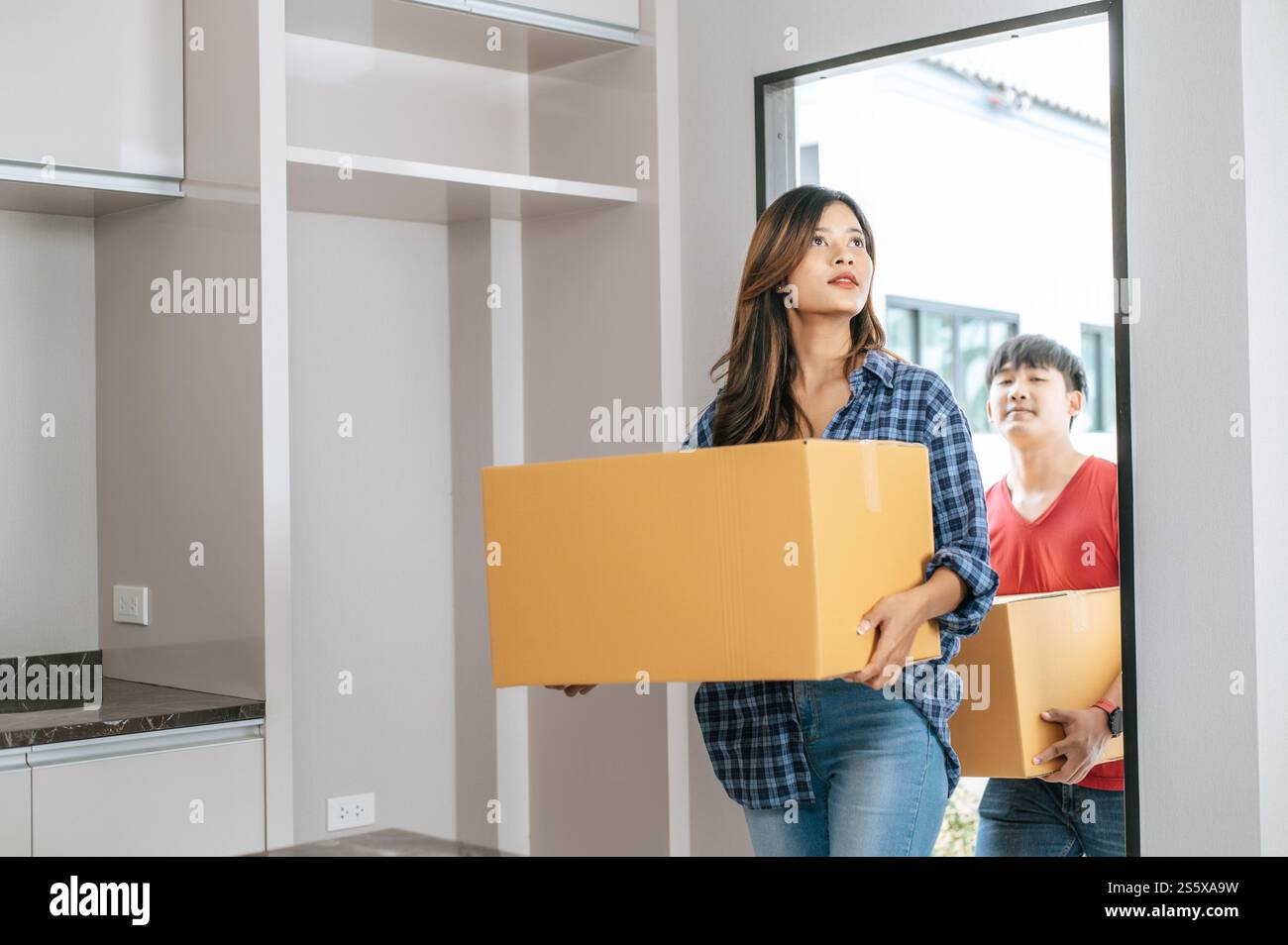 La giovane coppia asiatica aiuta a tenere una pesante scatola di cartone entra in una nuova casa con felicità, nuovo concetto di casa in movimento Foto Stock