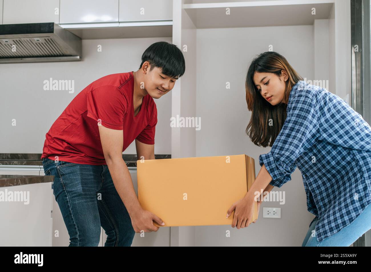 La giovane coppia asiatica aiuta a tenere una pesante scatola di cartone entra in una nuova casa con felicità, nuovo concetto di casa in movimento Foto Stock