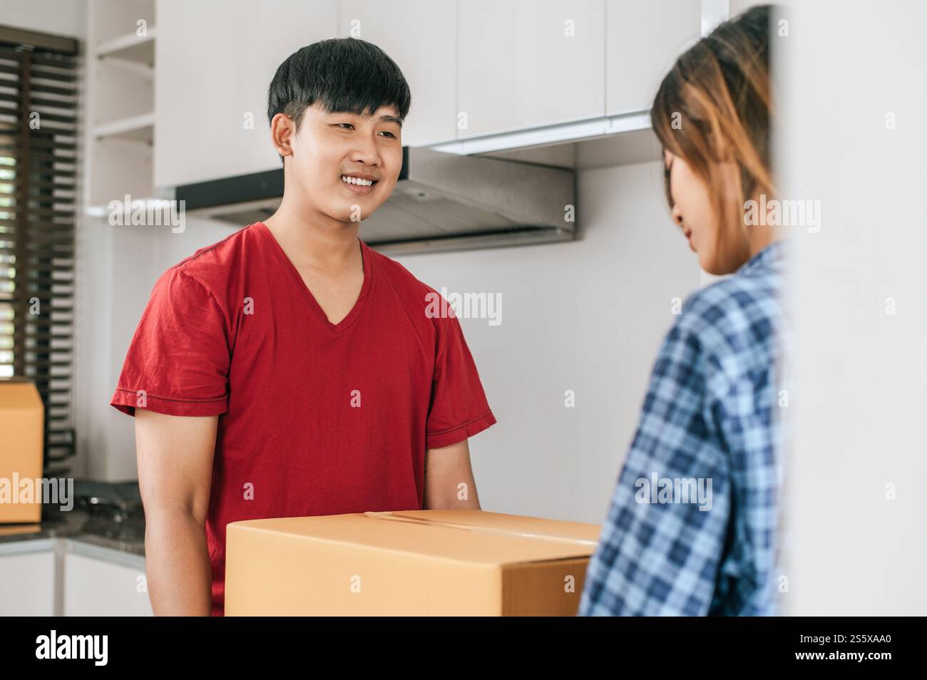 La giovane coppia asiatica aiuta a tenere una pesante scatola di cartone entra in una nuova casa con felicità, nuovo concetto di casa in movimento Foto Stock