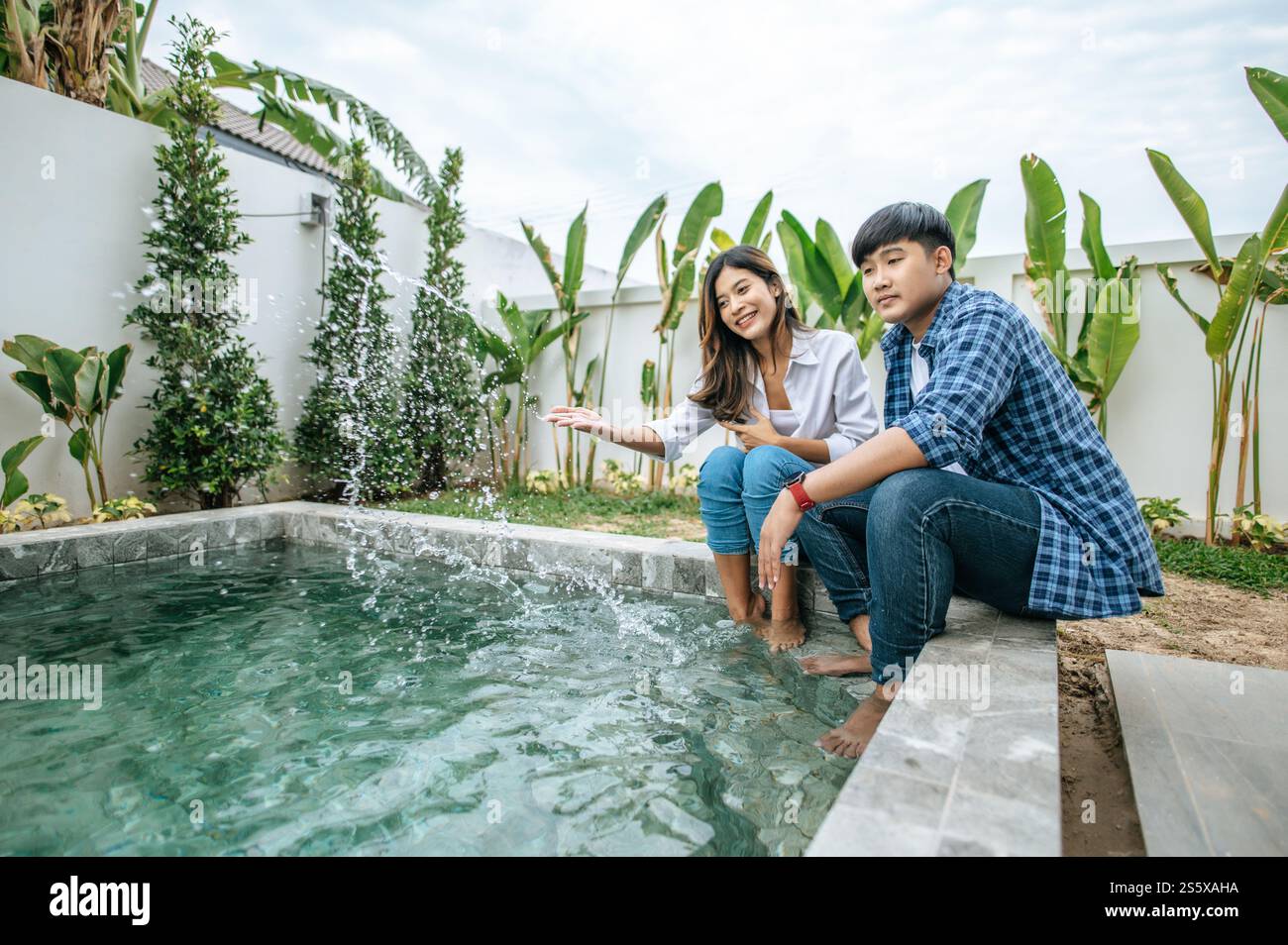 La giovane coppia asiatica si diverte insieme mentre riposa vicino alla piscina, nella nuova casa, il giovane e bello uomo abbraccia la spalla della moglie, concetto di famiglia felice Foto Stock