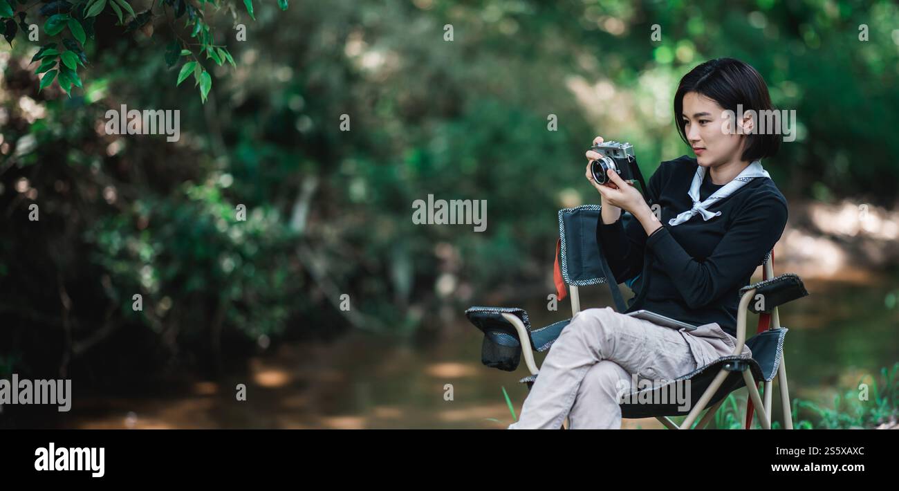 La giovane bella donna usa la fotocamera digitale per scattare una foto della splendida natura mentre campeggia nella foresta con felicità, copia spazio Foto Stock
