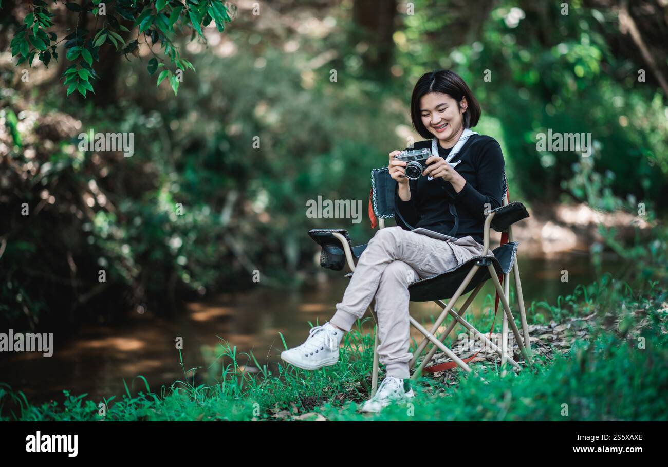 La giovane bella donna usa la fotocamera digitale per scattare una foto della splendida natura mentre campeggia nella foresta con felicità, copia spazio Foto Stock
