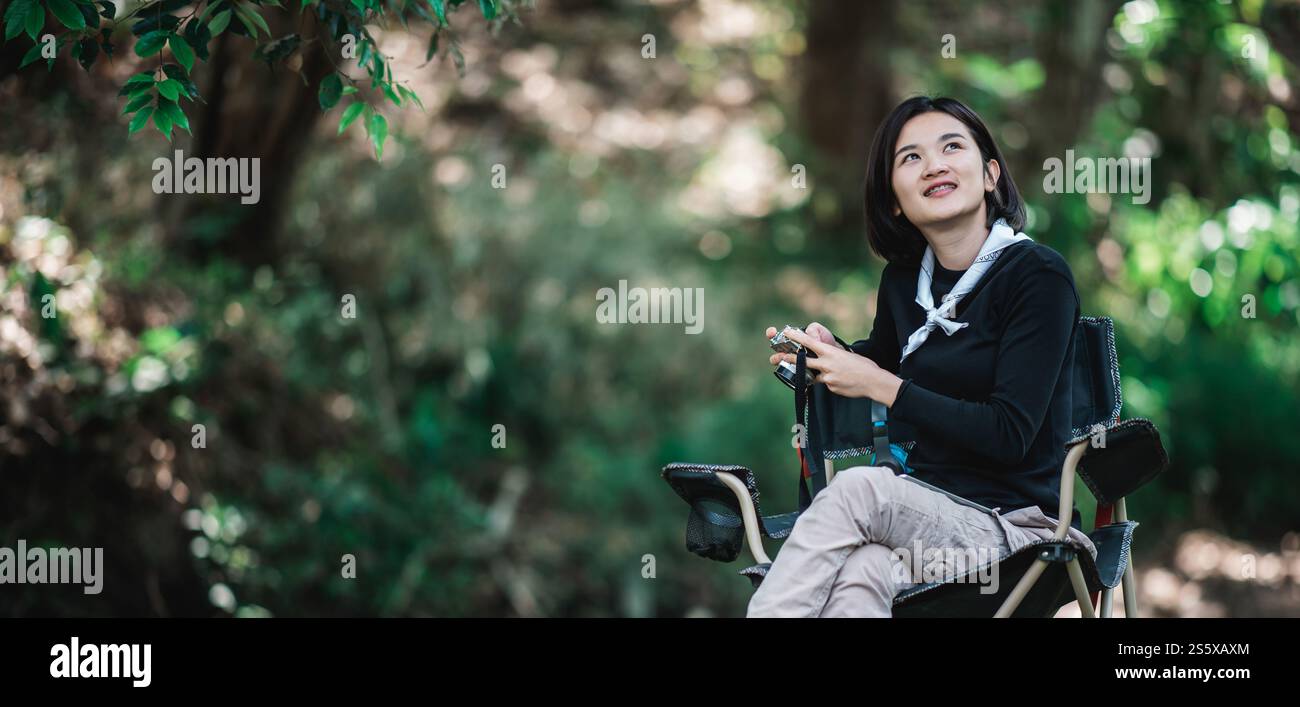 La giovane bella donna usa la fotocamera digitale per scattare una foto della splendida natura mentre campeggia nella foresta con felicità, copia spazio Foto Stock