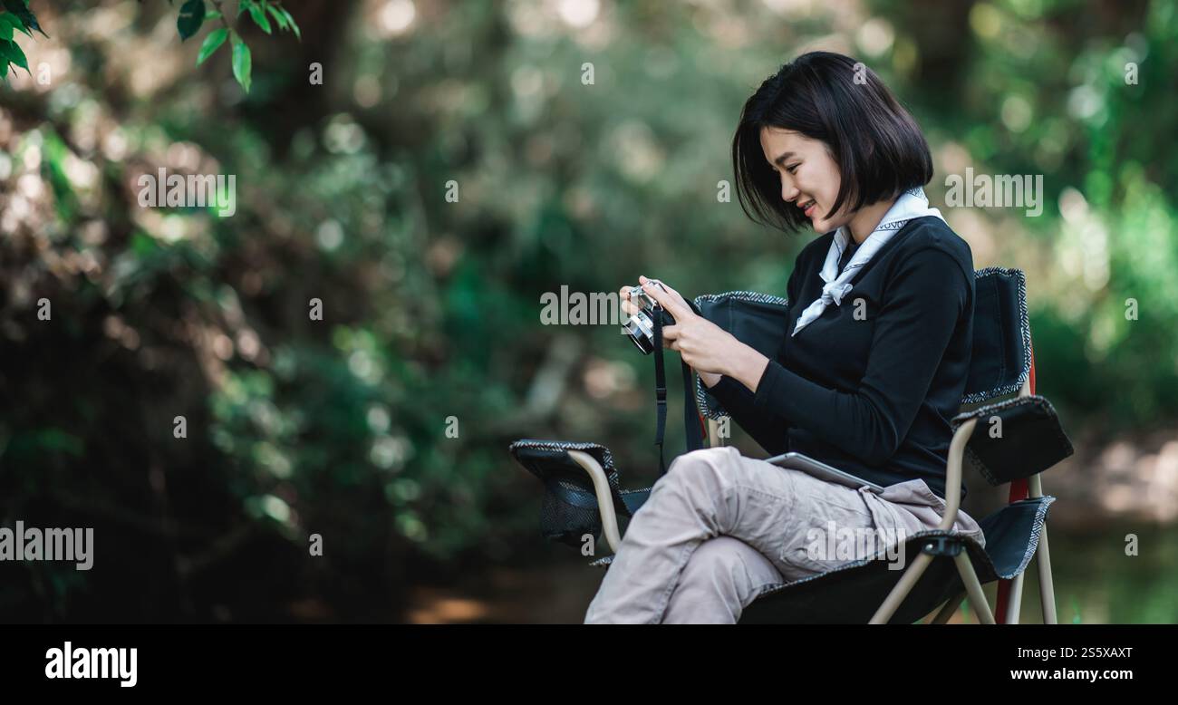 La giovane bella donna usa la fotocamera digitale per scattare una foto della splendida natura mentre campeggia nella foresta con felicità, copia spazio Foto Stock