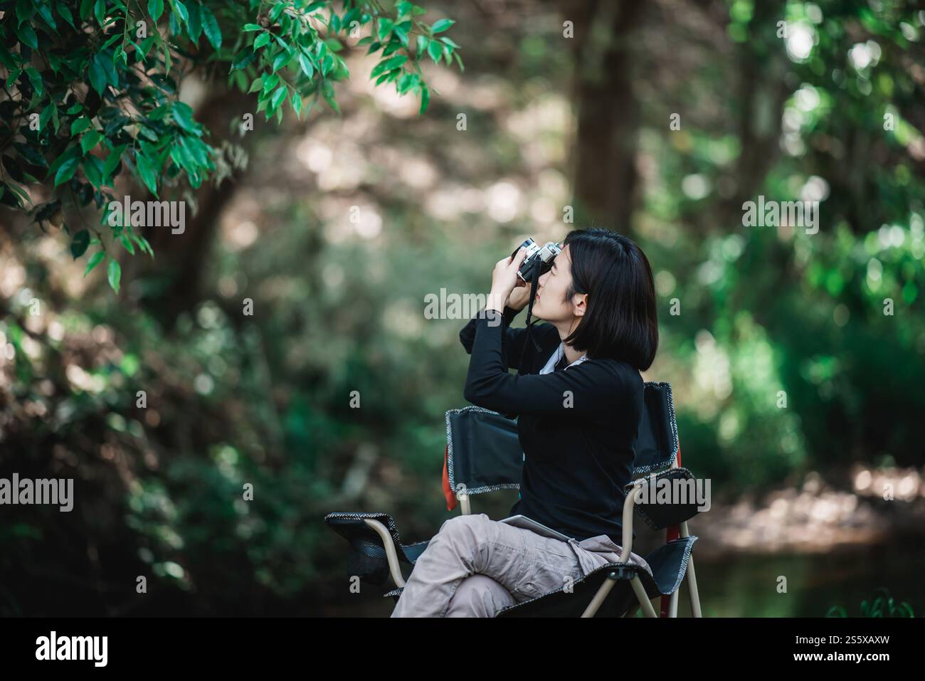 La giovane bella donna usa la fotocamera digitale per scattare una foto della splendida natura mentre campeggia nella foresta con felicità, copia spazio Foto Stock
