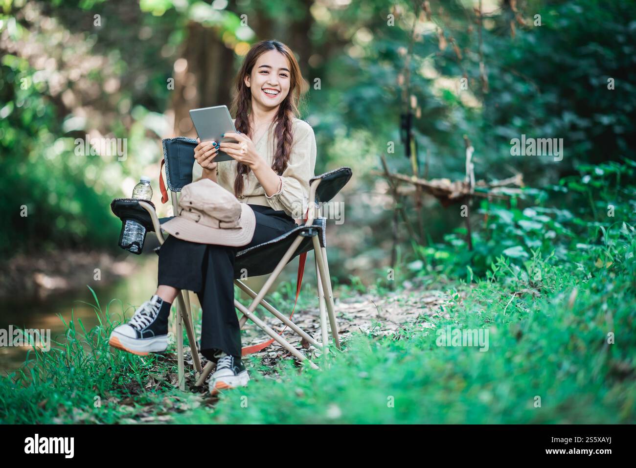 Giovane donna seduta su una sedia e utilizza una videochiamata con un tablet mentre campeggi nel parco naturale, spazio di copia Foto Stock