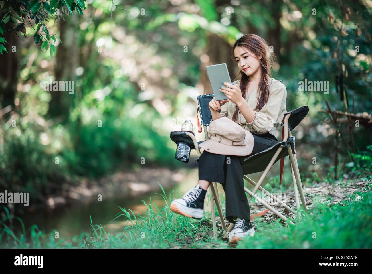 Giovane donna seduta su una sedia e utilizza una videochiamata con un tablet mentre campeggi nel parco naturale, spazio di copia Foto Stock
