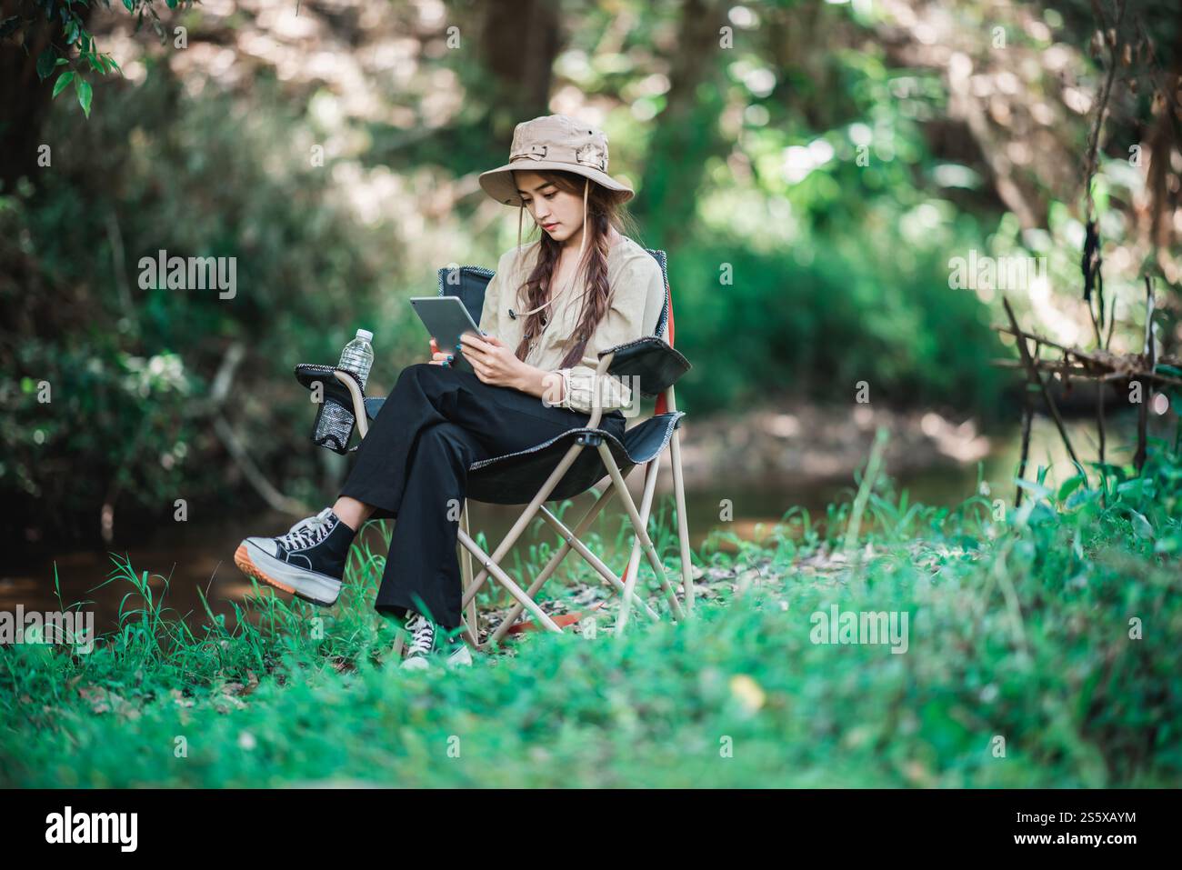 Giovane donna seduta su una sedia e utilizza una videochiamata con un tablet mentre campeggi nel parco naturale, spazio di copia Foto Stock