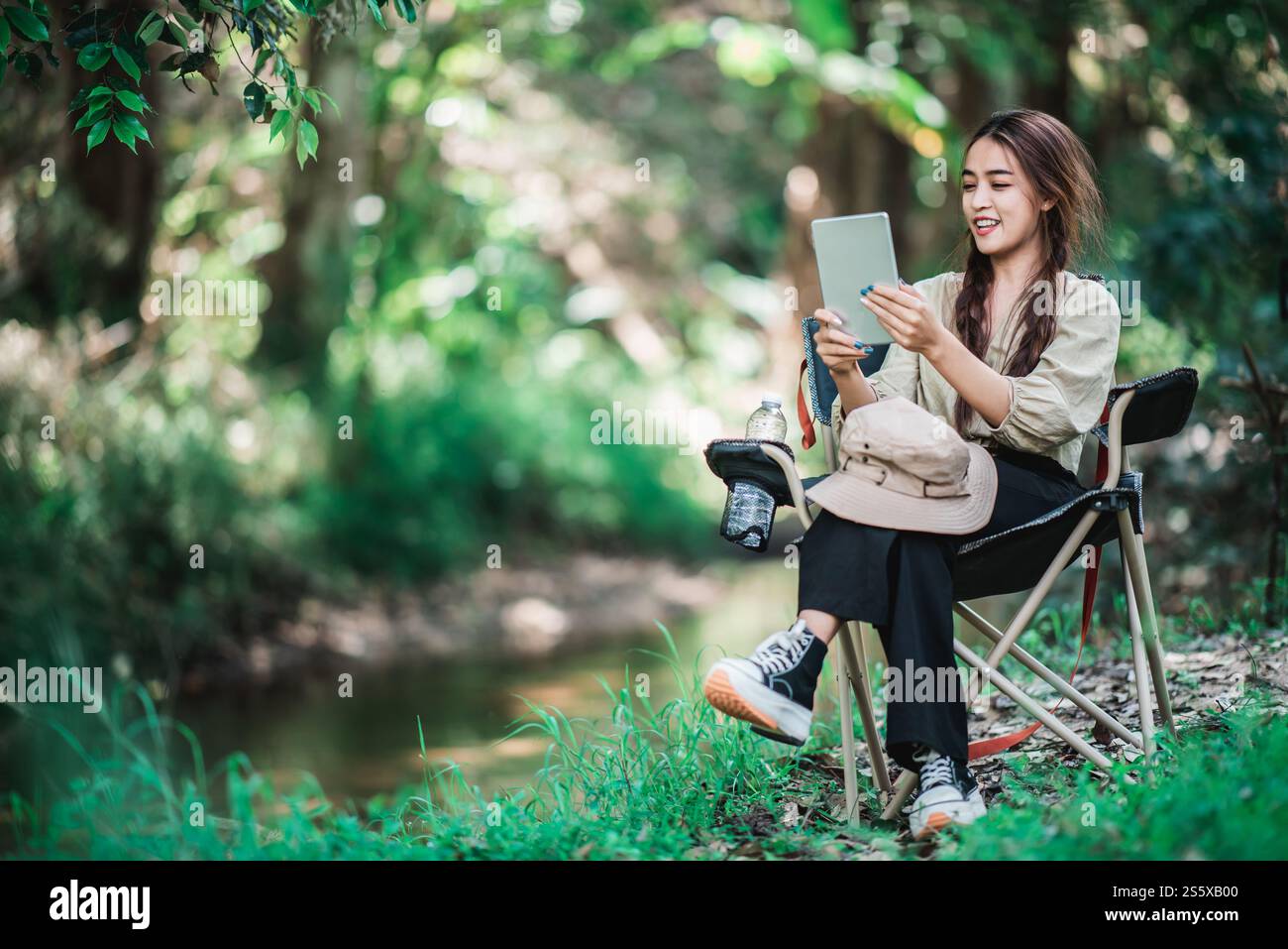 Giovane donna seduta su una sedia e utilizza una videochiamata con un tablet mentre campeggi nel parco naturale, spazio di copia Foto Stock
