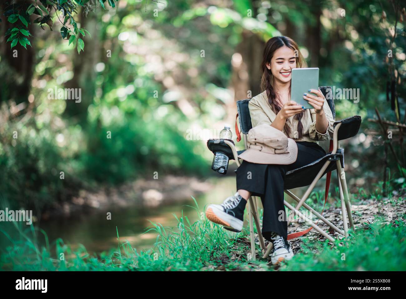 Giovane donna seduta su una sedia e utilizza una videochiamata con un tablet mentre campeggi nel parco naturale, spazio di copia Foto Stock