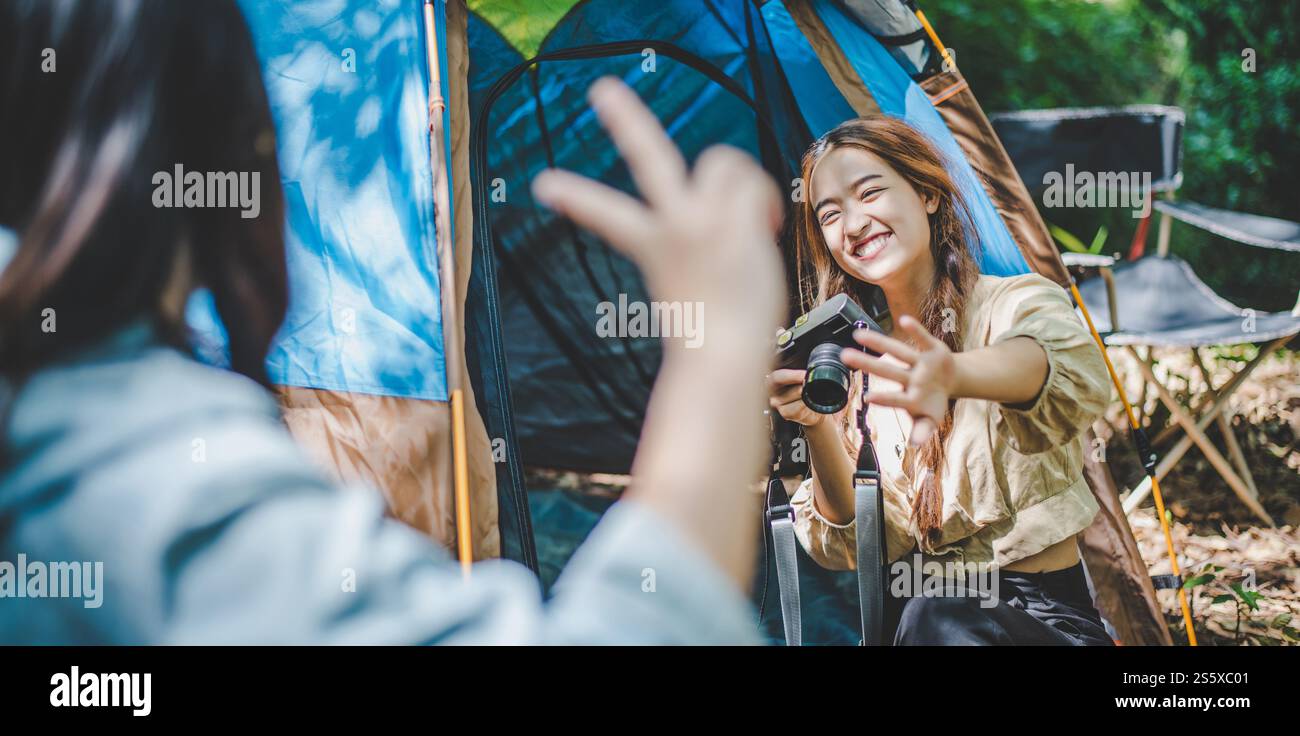 Giovane e graziosa fotografa con fotocamera digitale mentre si siede alla tenda da campeggio nella foresta, giovani donne asiatiche viaggiano in campeggio all'aperto. Foto Stock