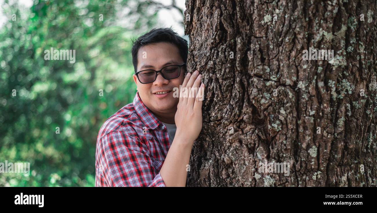 Ritratto di un uomo asiatico felice che abbraccia un albero nella foresta. Proteggere e amare la natura. Concetto di ambiente ed ecologia. Foto Stock