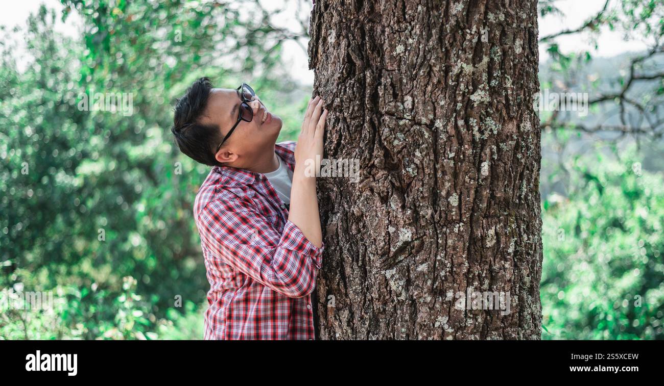 Ritratto di un uomo asiatico felice che abbraccia un albero nella foresta. Proteggere e amare la natura. Concetto di ambiente ed ecologia. Foto Stock