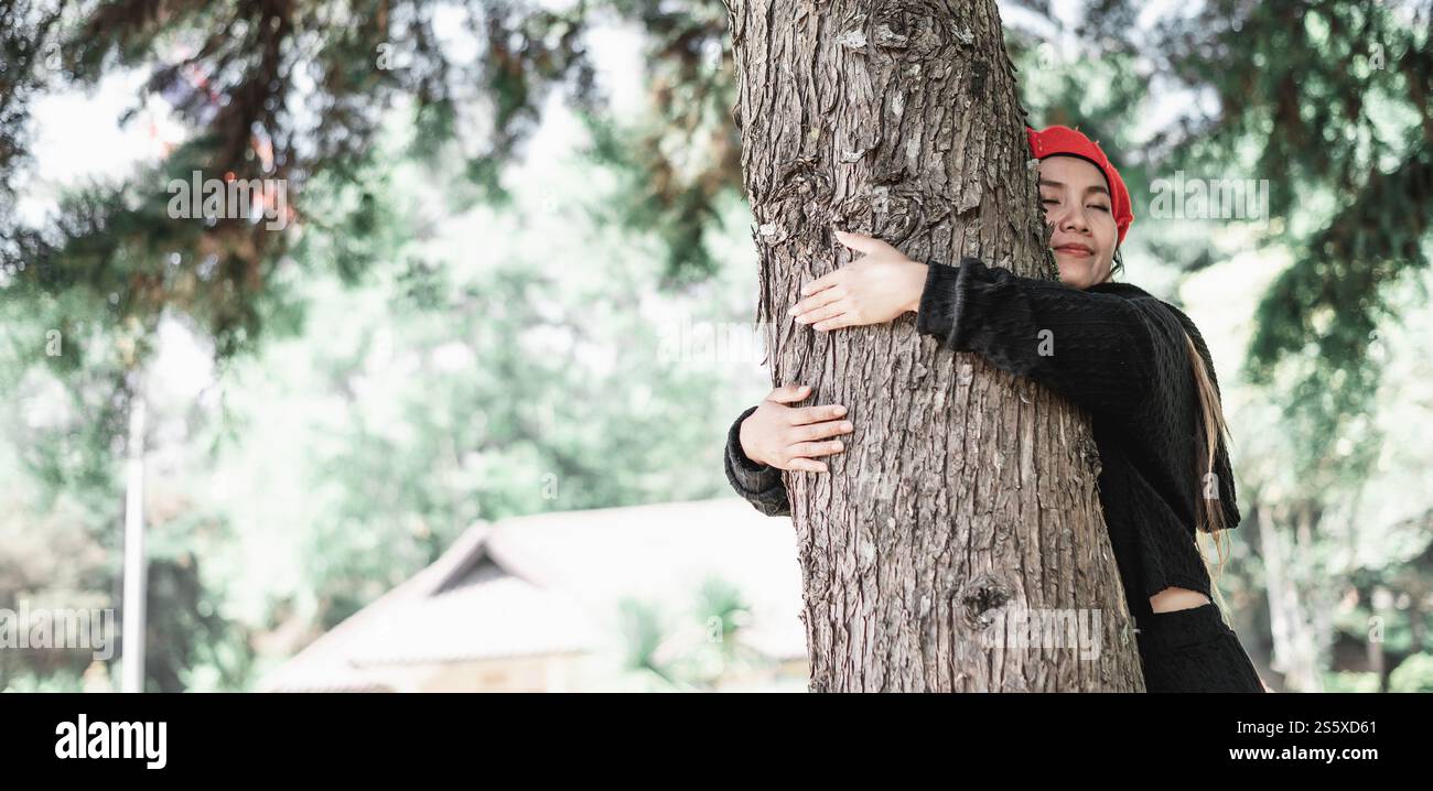 Giovane donna contenta che abbraccia un grande albero con un'espressione beata con spazio di copia. Concetto di cura per l'ambiente. Foto Stock