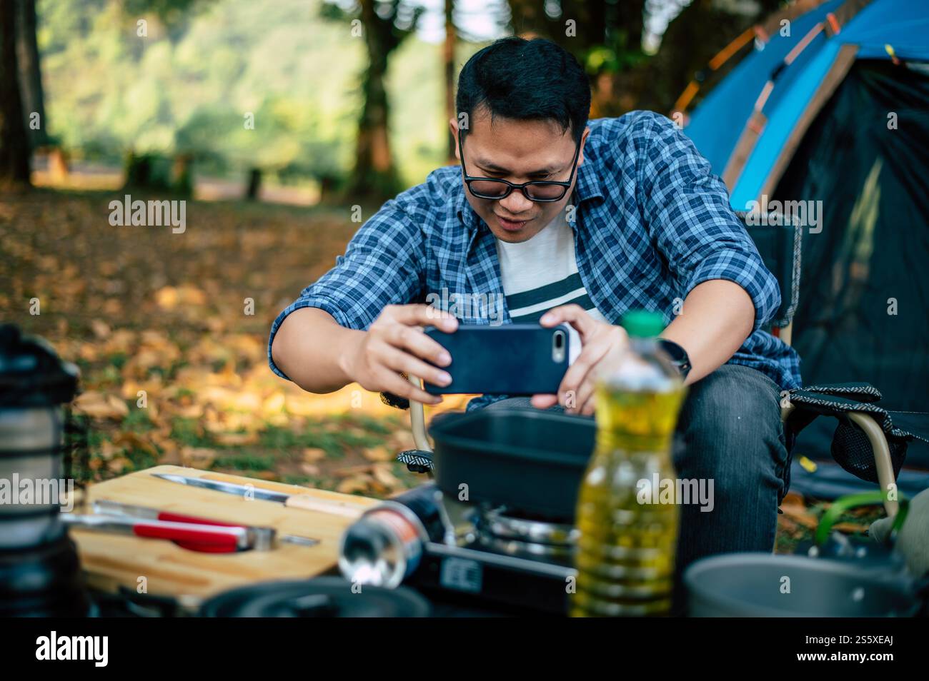 Ritratto di uomini viaggiatori asiatici che scattano una foto su smartphone in campeggio. Cucina all'aperto, viaggi, campeggio, stile di vita. Foto Stock