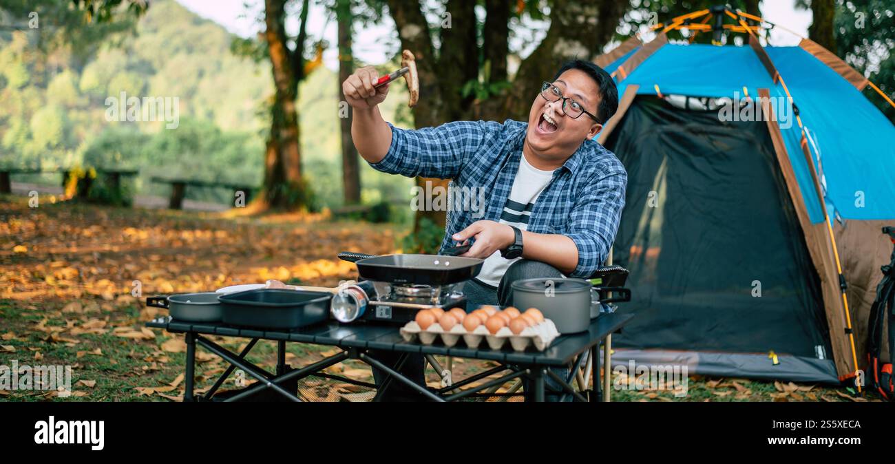 Ritratto dell'uomo viaggiatore asiatico che prepara una bistecca di maiale, barbecue in padella arrostita o pentola in campeggio. Cucina all'aperto, viaggi, campeggio, Foto Stock