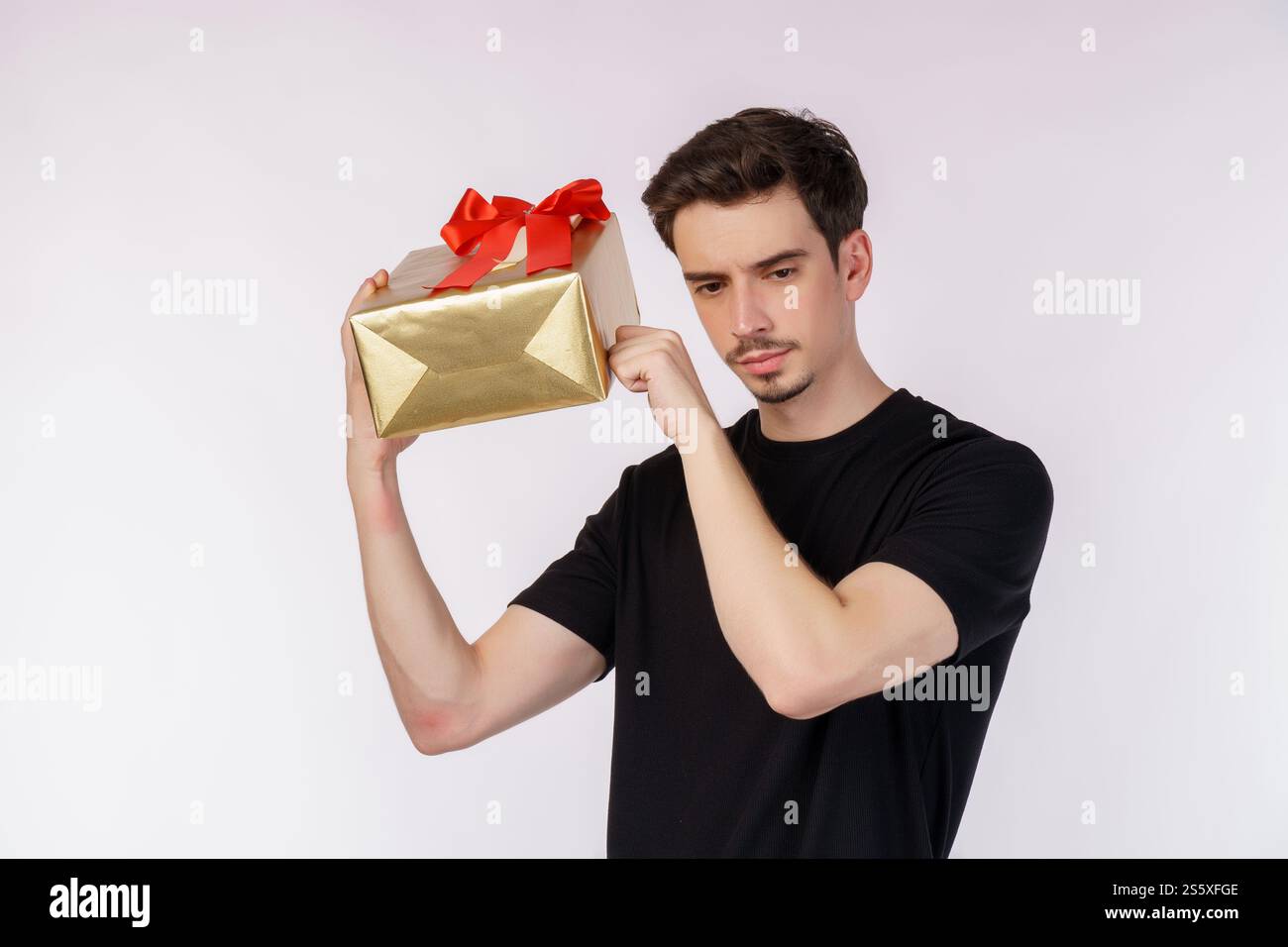 Ritratto di un giovane uomo caucasico confuso che mostra la scatola presente e guarda la fotocamera isolata su sfondo bianco. Concetto di festa di compleanno. Foto Stock