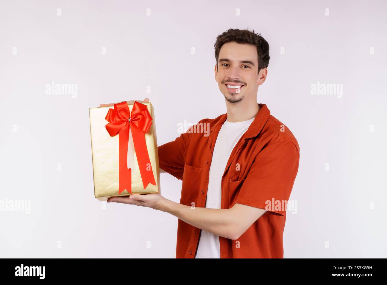 Ritratto di felice giovane uomo caucasico che mostra la scatola presente e guarda la macchina fotografica isolata su sfondo bianco. Concetto di festa di compleanno. Foto Stock