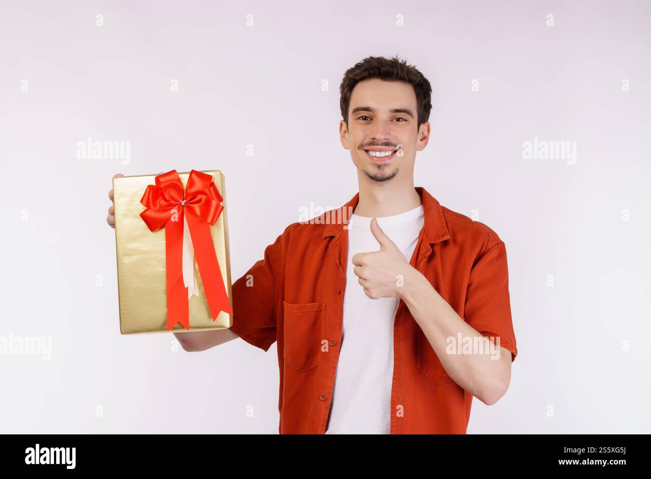 Ritratto di felice giovane uomo caucasico che mostra la scatola presente e guarda la macchina fotografica isolata su sfondo bianco. Concetto di festa di compleanno. Foto Stock