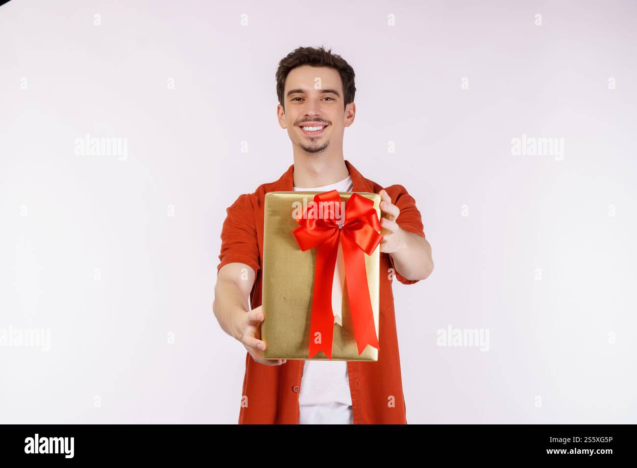 Ritratto di felice giovane uomo caucasico che mostra la scatola presente e guarda la macchina fotografica isolata su sfondo bianco. Concetto di festa di compleanno. Foto Stock