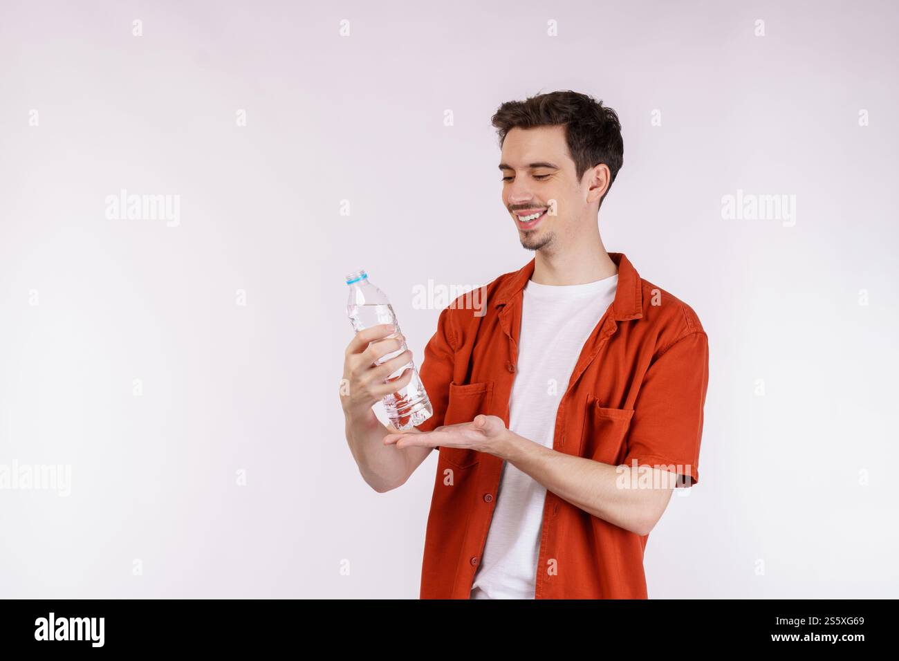 Ritratto di un giovane felice che mostra l'acqua in una bottiglia isolata su sfondo bianco. Alimentazione sana, dieta e concetto di persone. Foto Stock