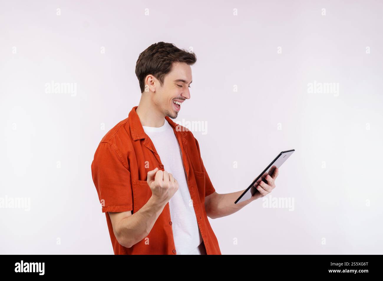 Ritratto di un uomo attraente e allegro che fa il gesto vincente stringendo il pugno e utilizzando l'app per dispositivi che cerca in rete isolata su sfondo bianco. Foto Stock