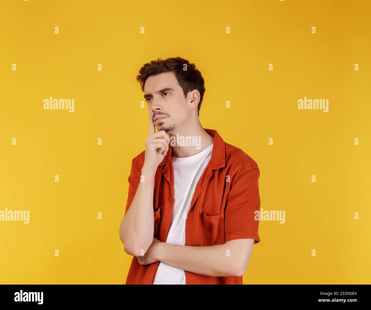 Ritratto di un giovane che pensa toccando il mento isolato su sfondo giallo. Pensare preoccupato per una domanda, preoccupato e nervoso con la mano sopra Foto Stock