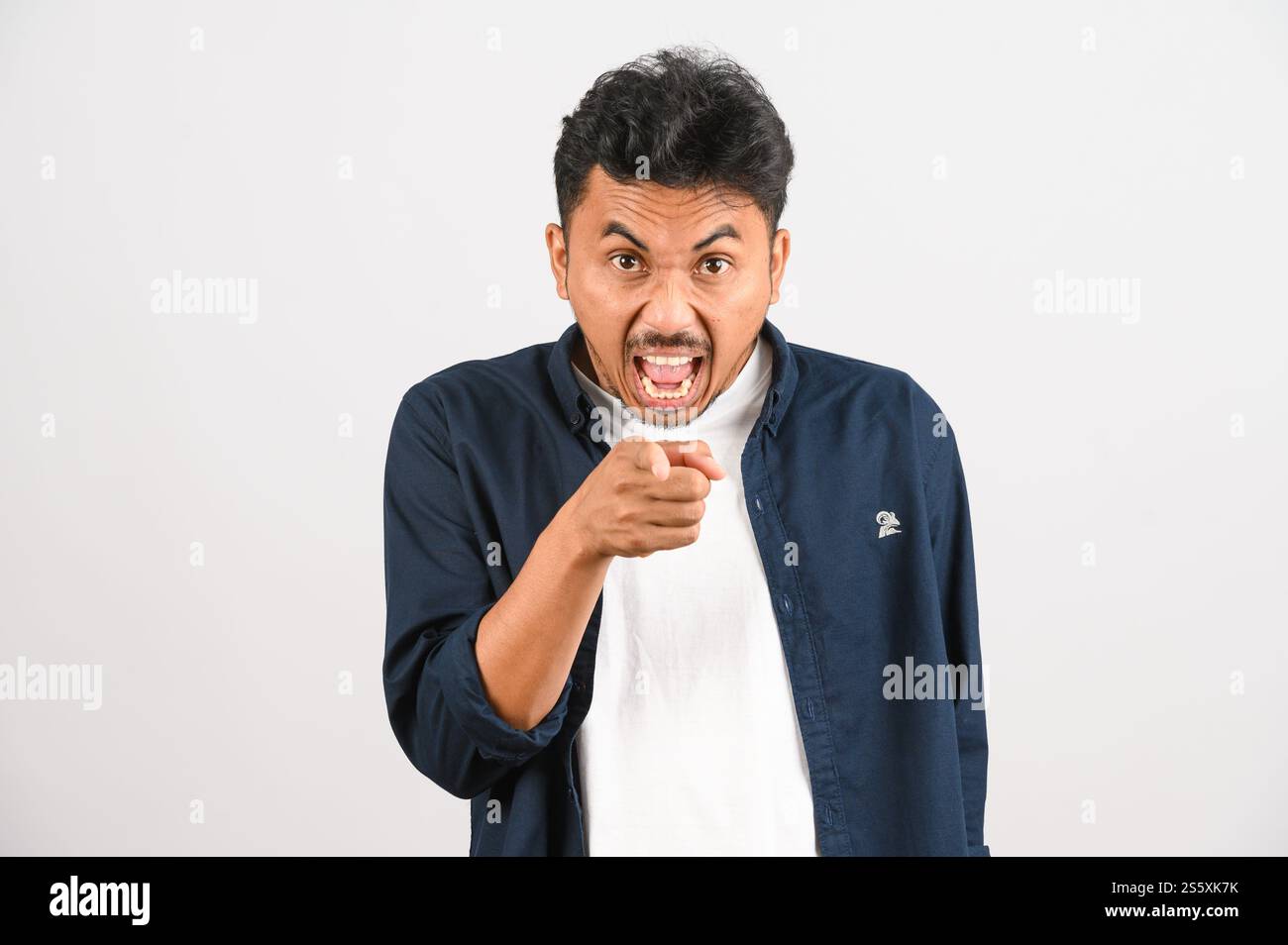 Ritratto di un giovane asiatico in camicia blu che punta verso la macchina fotografica isolata su sfondo bianco. Concetto di espressione e stile di vita. Foto Stock